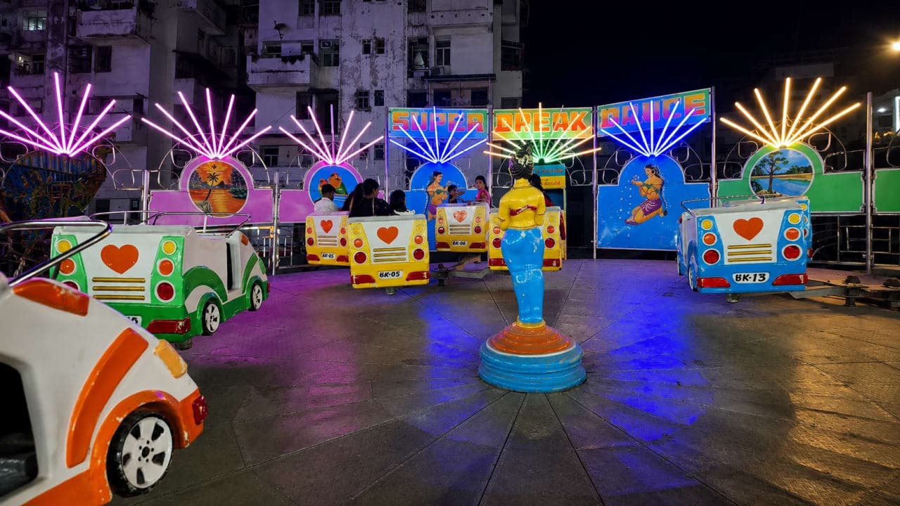 Colourfully illuminated Break Dance ride at the seasonal Disneyland fair in Patna at night, featuring brightly painted ride cars, neon lights, and visitors enjoying the attraction.