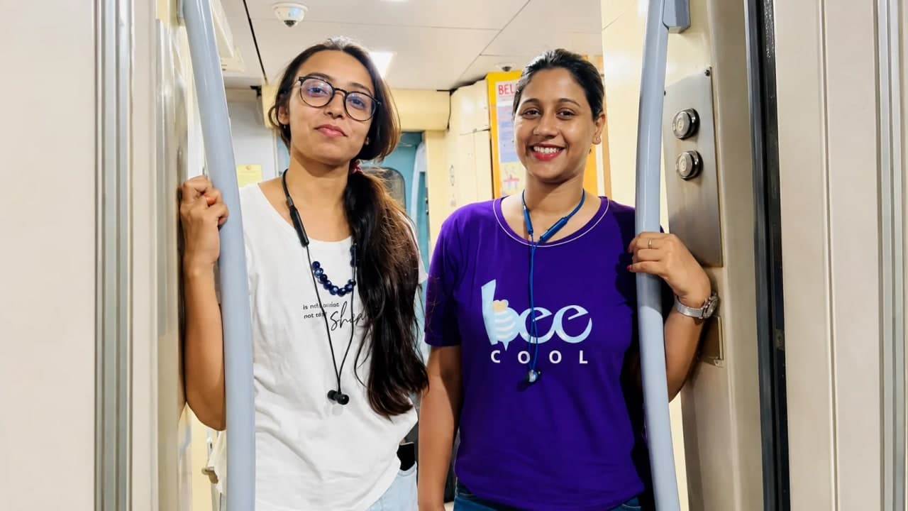 Two longtime school friends standing in the doorway of a train coach during their journey from Patna to Delhi, smiling for a photograph as they begin a memorable summer trip together.