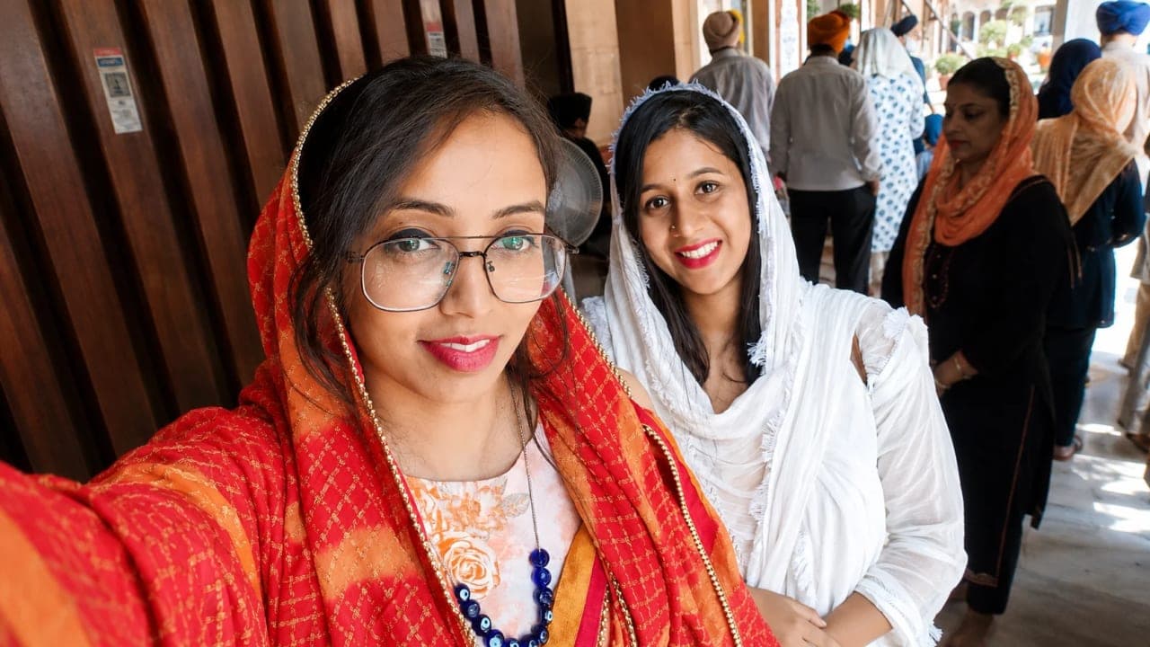 Two friends posing for a selfie inside Gurudwara Sis Ganj Sahib in Delhi, wearing head coverings and traditional attire while visiting the historic Sikh shrine during their summer trip.