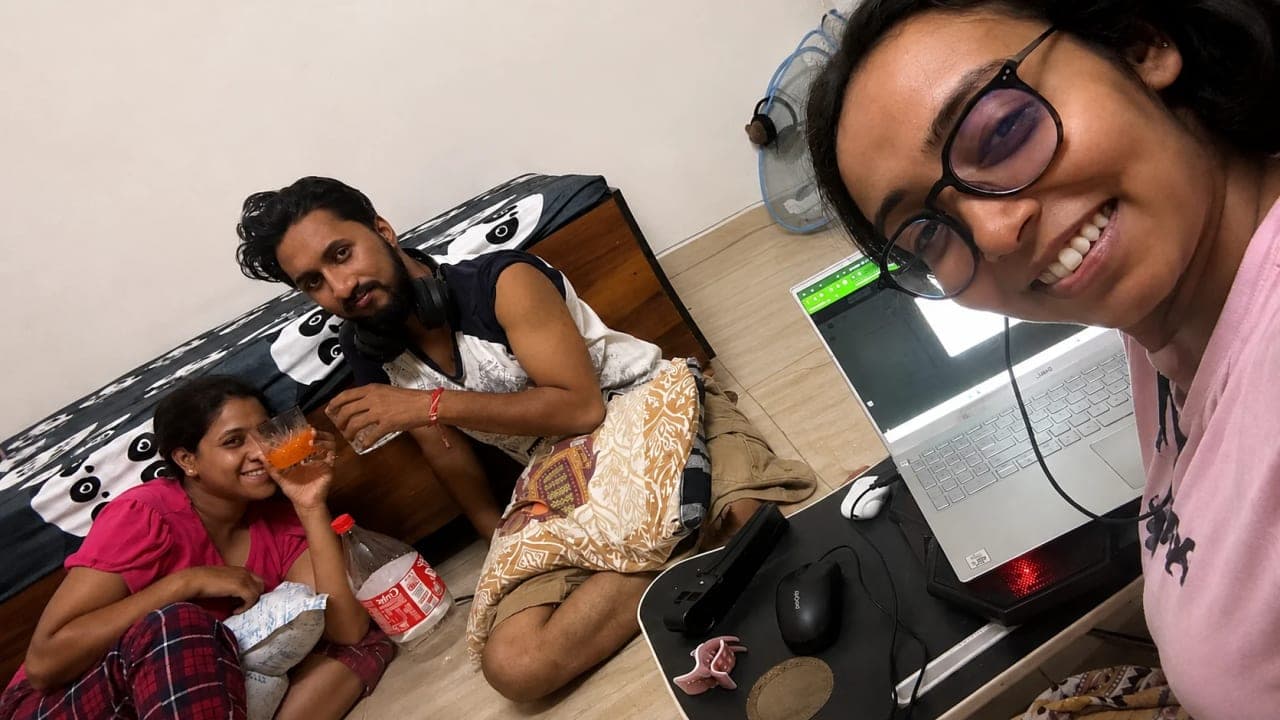 Three friends relaxing at home during a late-night gathering, sharing drinks, conversations, and laughter while one of them balances office work on a laptop. The evening was part of a memorable week before their upcoming trip, filled with friendship, fun, and sleepless adventures.