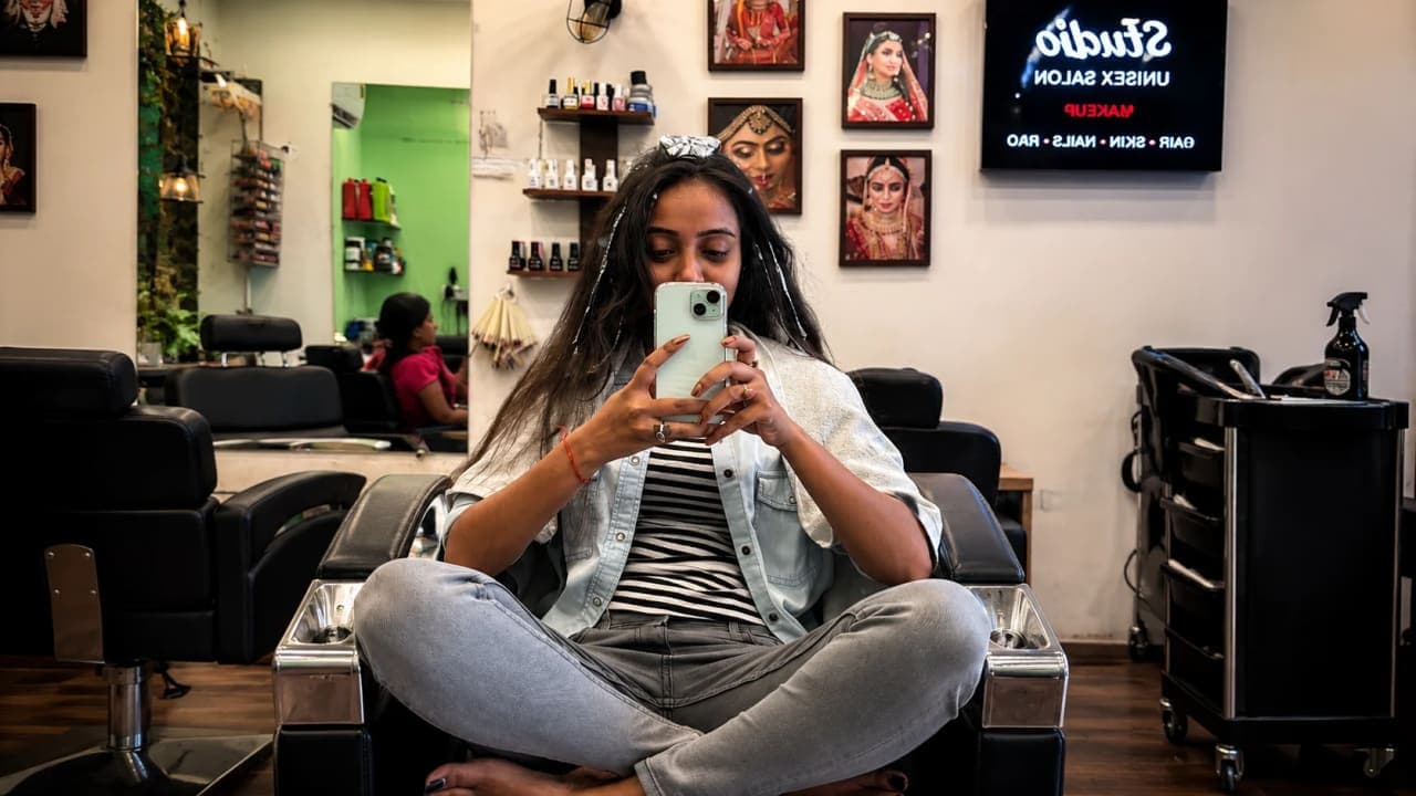 A woman sitting in a salon chair during a hair-highlighting session, taking a mirror selfie while foil wraps are applied to her hair. The makeover was part of a pre-trip preparation day spent with her husband and school friend before embarking on their long-awaited journey.