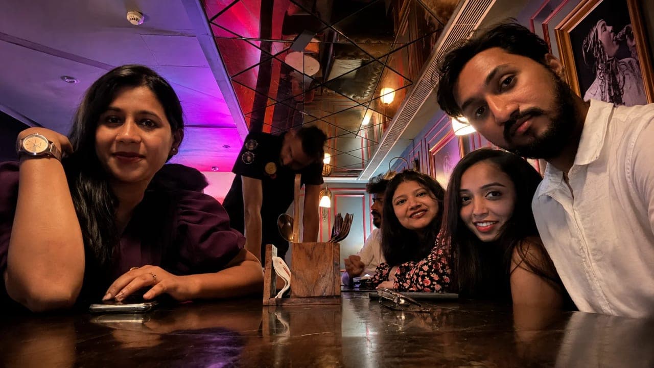 Friends gathered around a restaurant table during a first wedding anniversary celebration, smiling for a group photograph before beginning their long-awaited trip. The evening was filled with food, laughter, and celebrations that marked the perfect end to a memorable week together.