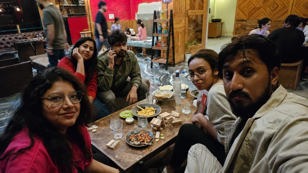 Friends gathered around a table in the hotel common hall at Jibhi, enjoying dinner, games, and conversations after a day of exploring the mountains.