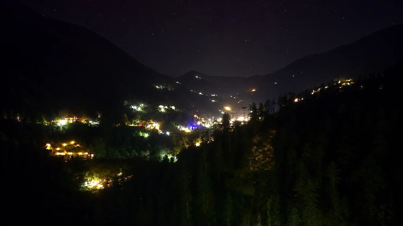 Night view of Jibhi valley from a hotel, with scattered lights glowing across the mountains under a starry sky.