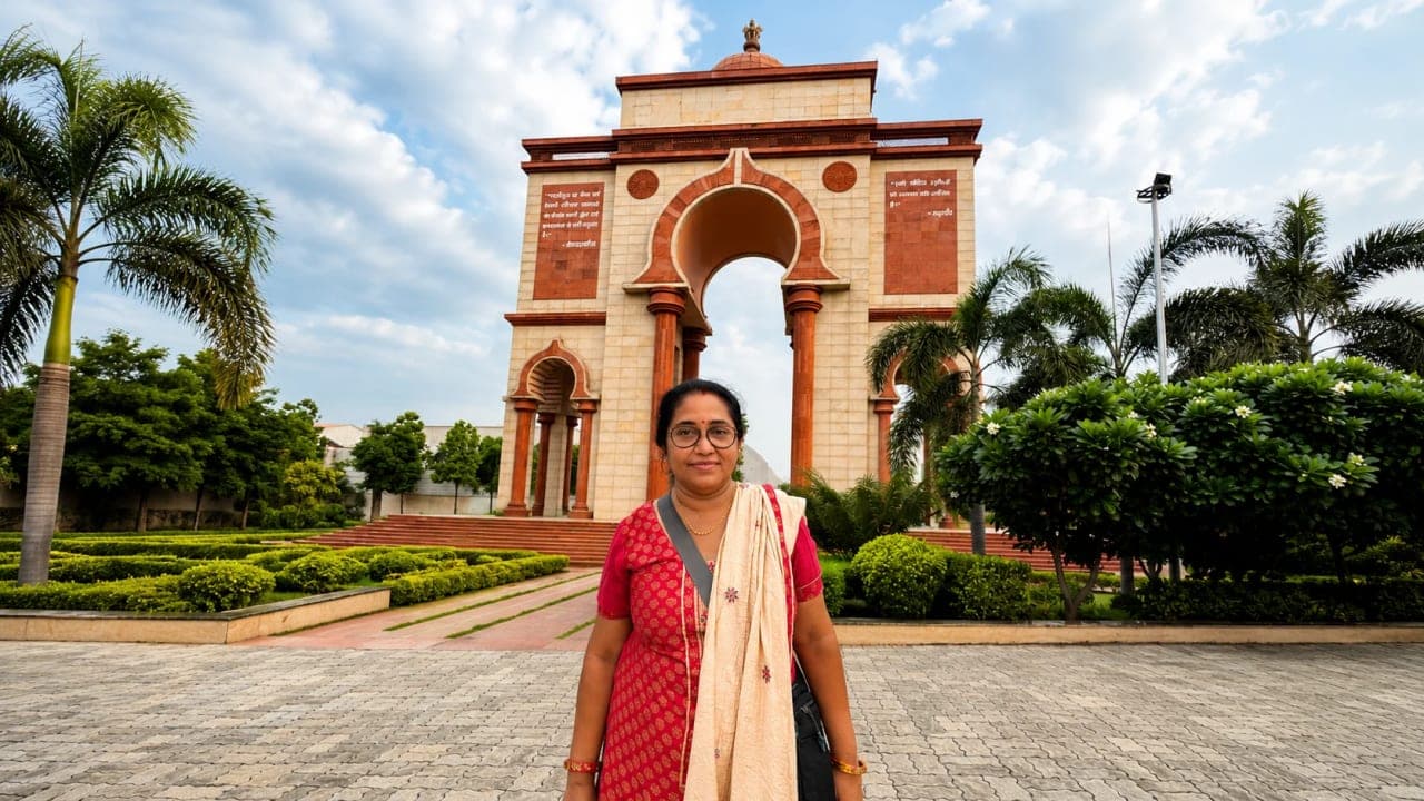 A woman posing in front of Sabhyata Dwar in Patna, with the grand sandstone monument and landscaped gardens visible in the background.