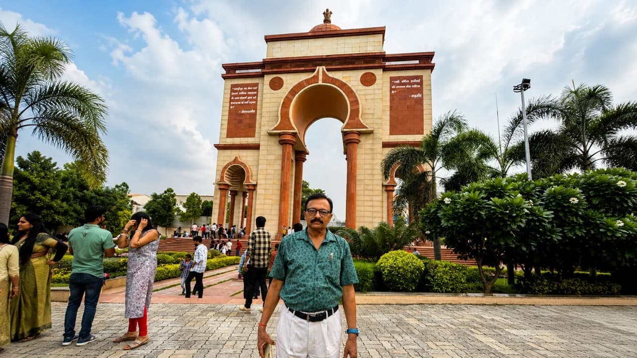 A man standing in front of Sabhyata Dwar in Patna, Bihar, with the grand sandstone monument, gardens, and open plaza visible in the background.