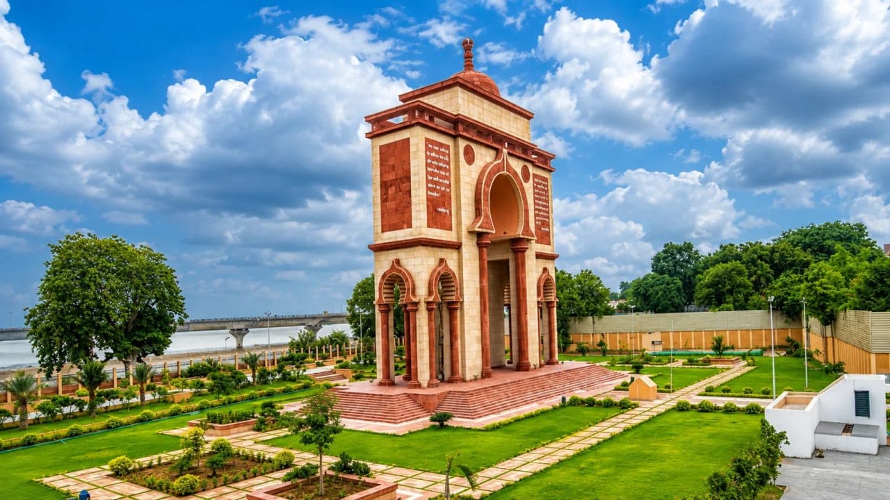 Wide view of Sabhyata Dwar in Patna, Bihar, standing amid landscaped gardens with the Ganga River and cloudy sky in the background.