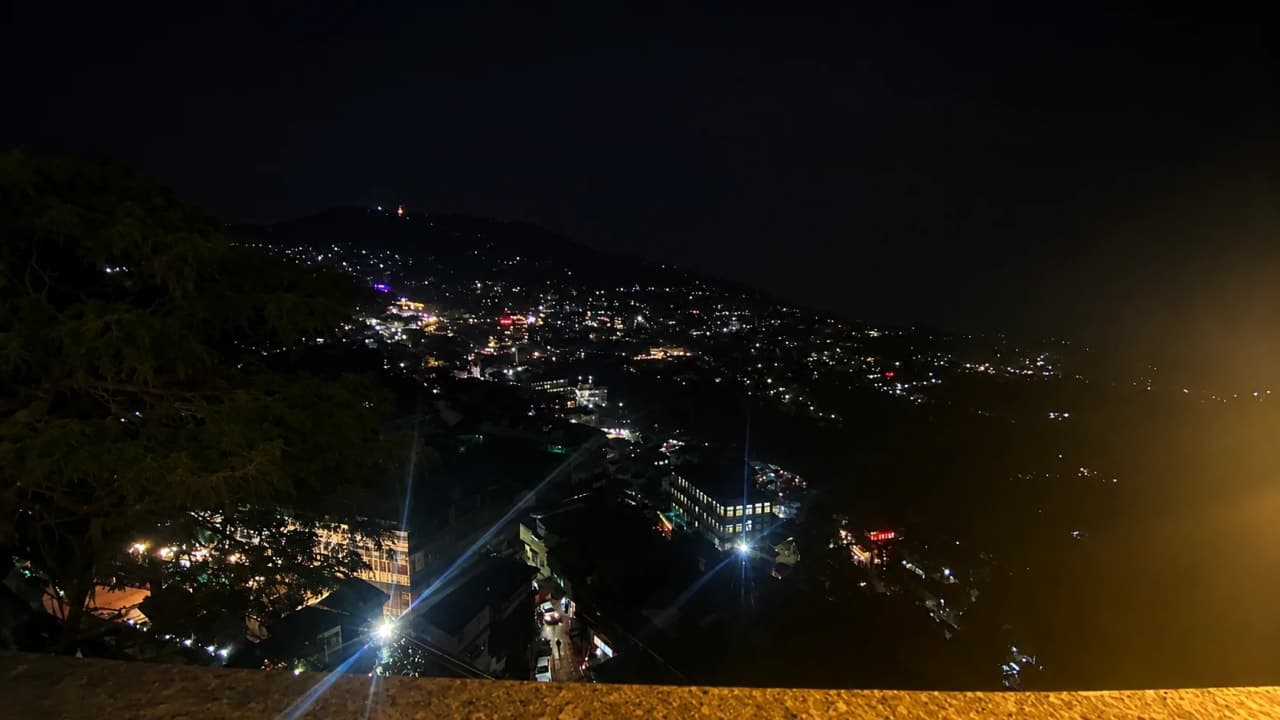 Night view of a hill town glowing with lights across the mountains.