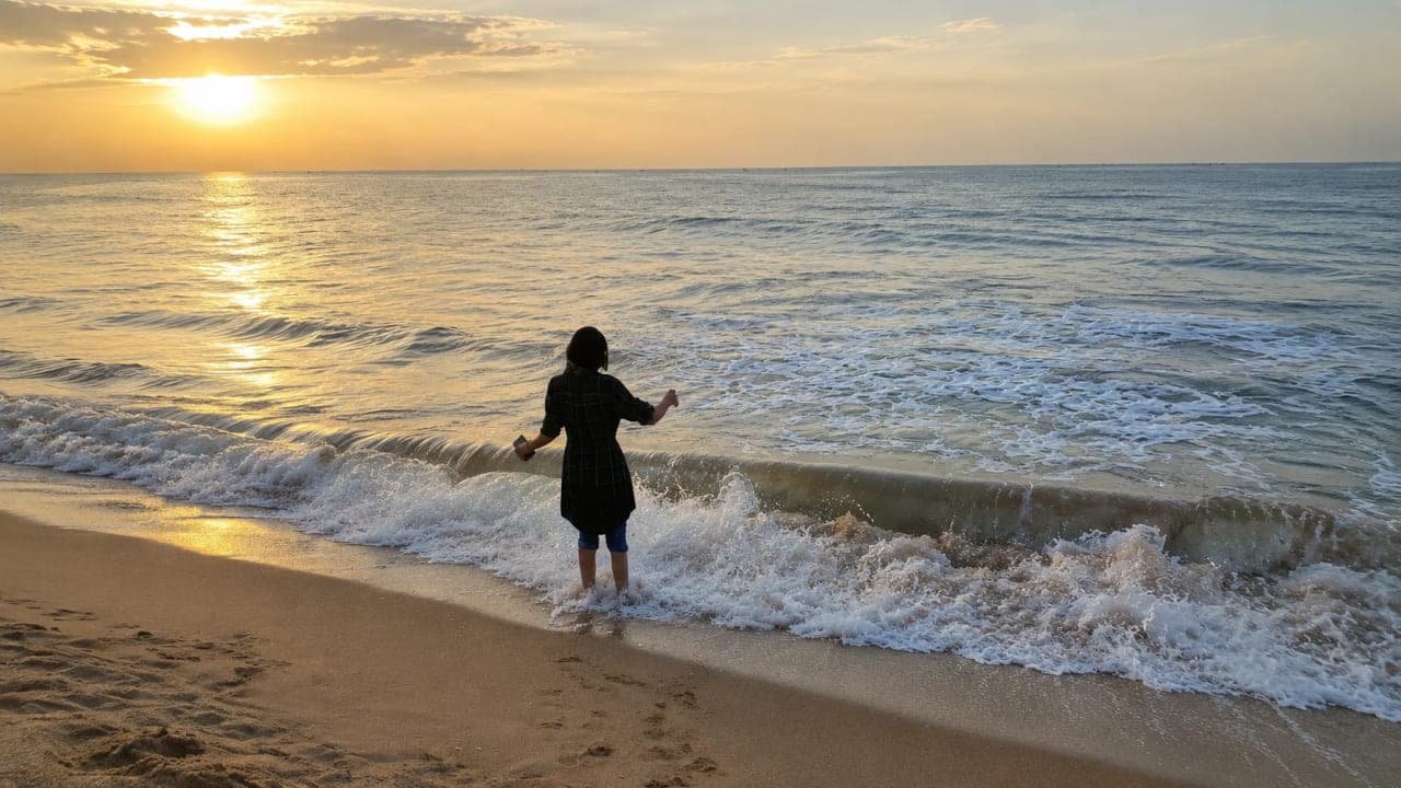 Girl relaxing on the beach at Auro Beach, Pondicherry, as the morning sky reflects over the calm ocean.