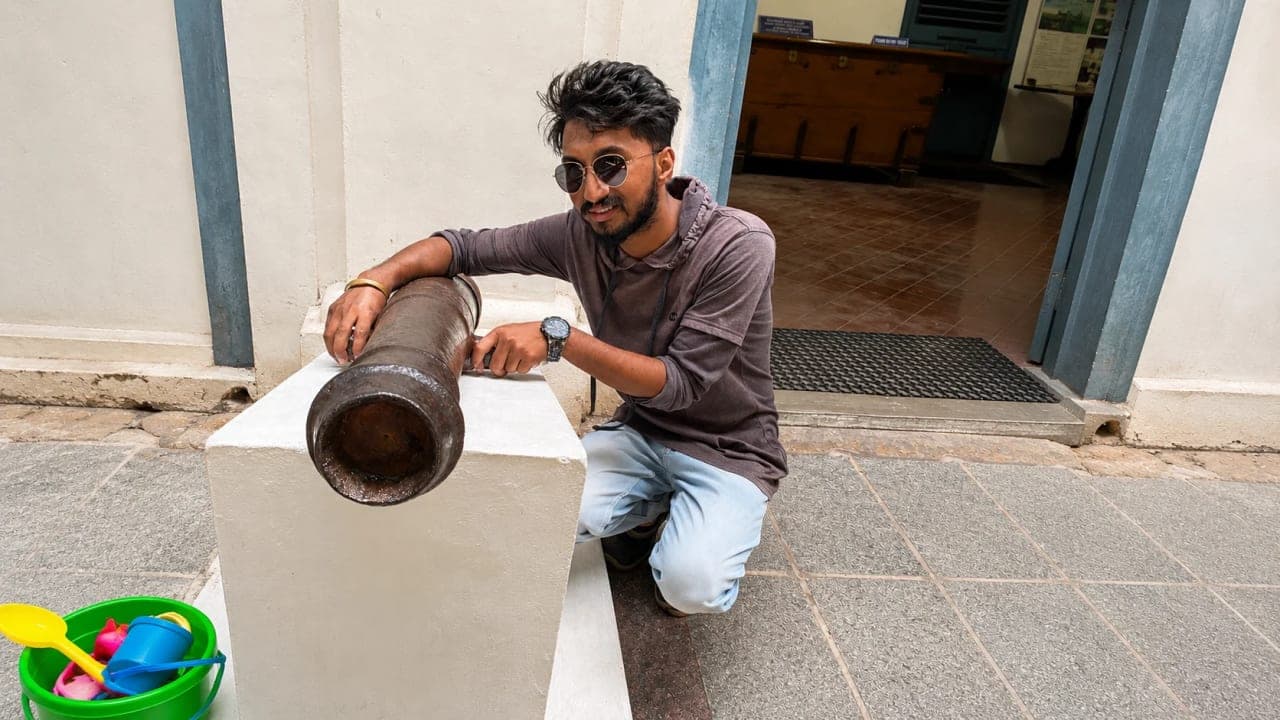 Visitor posing beside a historic cannon displayed at the Puducherry Museum.