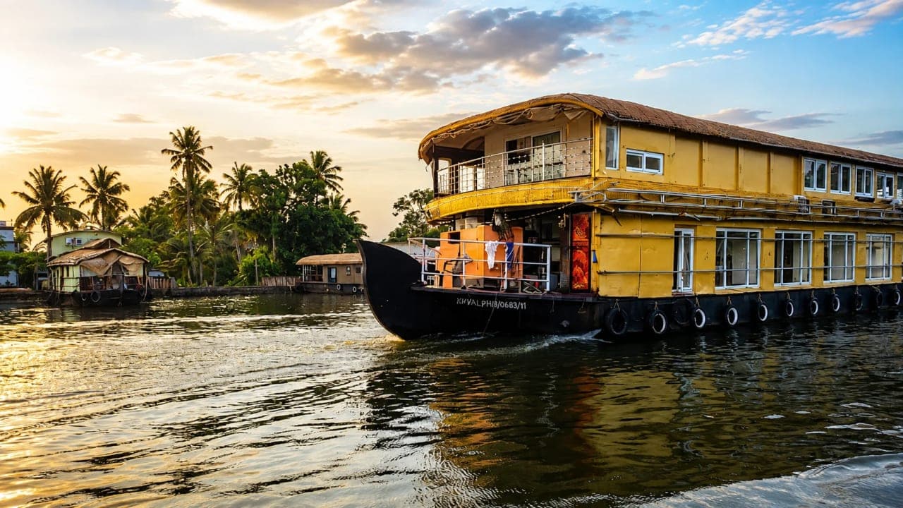 Traditional Kerala houseboat cruising through the peaceful backwaters of Alleppey, surrounded by coconut trees and lush greenery.