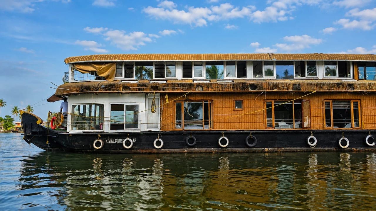 Traditional Kerala houseboat cruising through the serene backwaters of Alleppey, surrounded by coconut trees and calm waters.