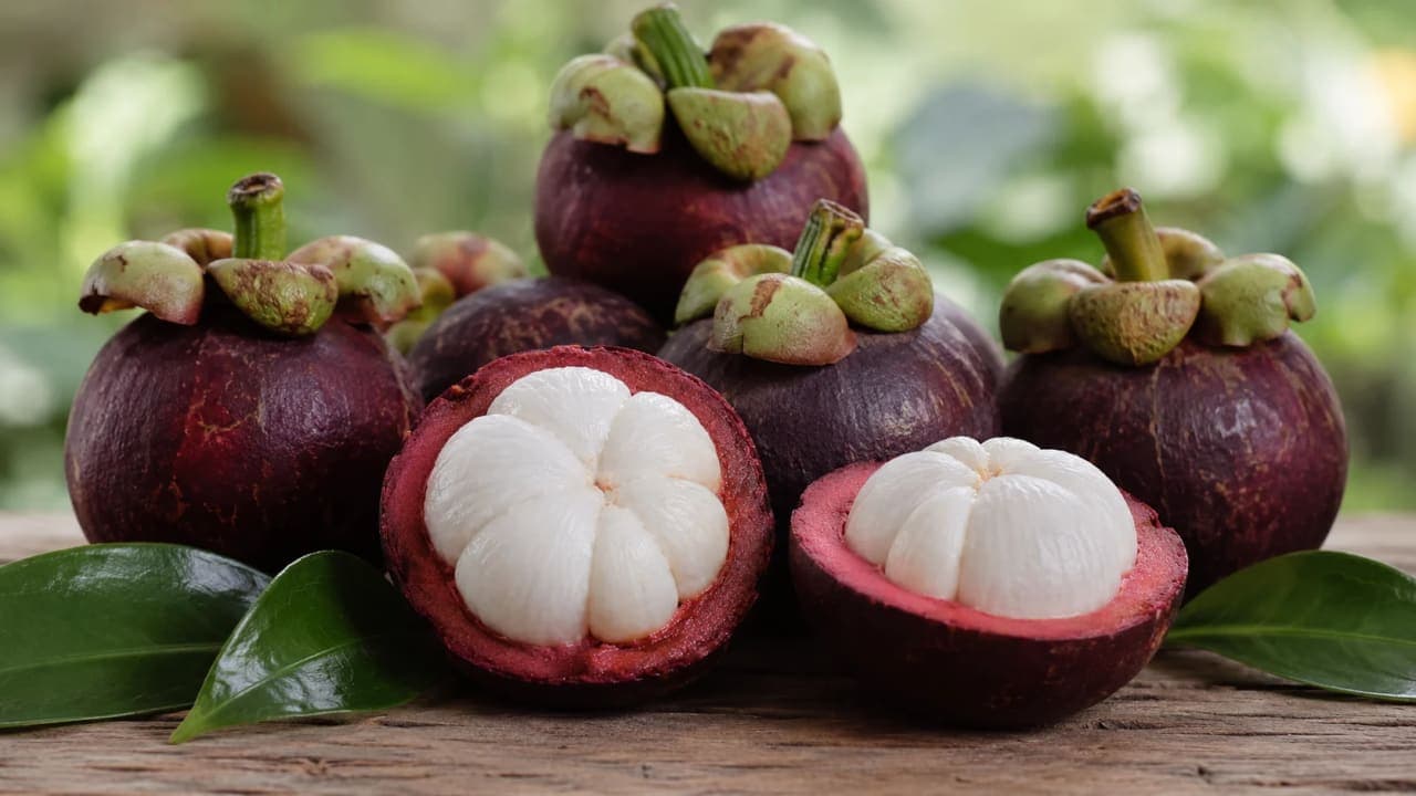 Fresh mangosteen fruits with deep purple rinds and soft white segmented flesh displayed after being cut open.