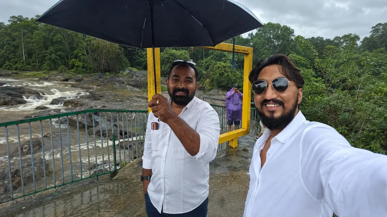My husband and our driver bhaiya posing together under an umbrella beside a rain-filled stream during our final day of the Kerala road trip.